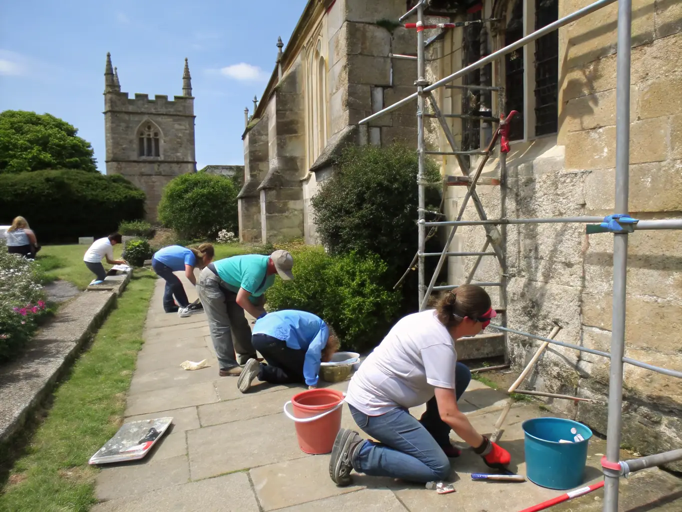 A photograph of a group of volunteers working on the restoration of a historical building facade, carefully cleaning and repairing the stonework.